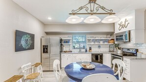 Een moderne keuken met witte kastjes, een blauwe eettafel en een kroonluchter.