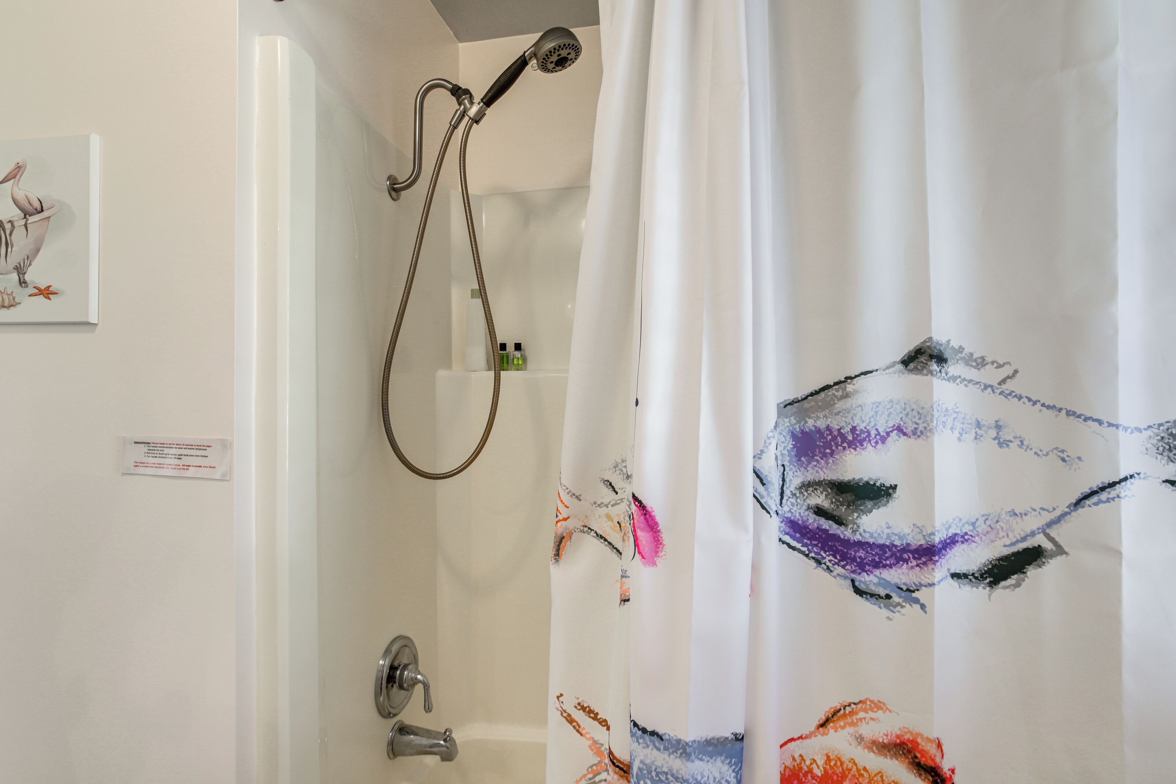 A bathroom with a shower, a toilet, and a sink. There is a painting on the wall and a shower curtain with a colorful design.