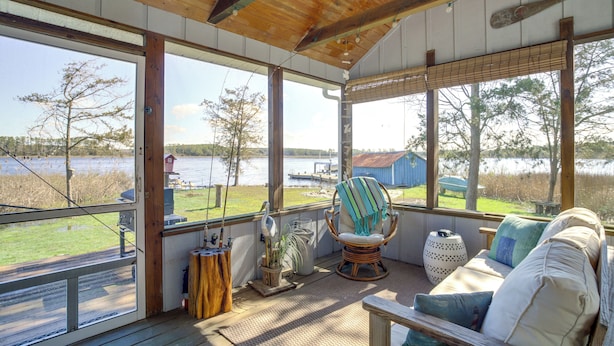 A covered porch with a view of a lake, a rocking chair, a cushioned bench, and a wooden table. - Dog-friendly Westover Cottage w/ River Access! (Westover)