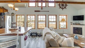 A spacious living area with a high ceiling, large windows, a cozy sofa, a wooden dining table, and a fireplace. - Dog-friendly Westover Cottage w/ River Access! (Westover)