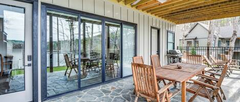 A covered patio with stone flooring, wooden furniture, and large sliding glass doors.
