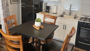 Una cocina moderna con un refrigerador negro, armarios blancos, una mesa de comedor con cuatro sillas de madera y una estufa negra.