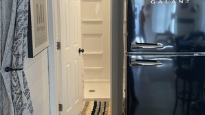 Una cocina con un refrigerador Galanz negro, techo de madera y una puerta blanca que da a otra habitación.
