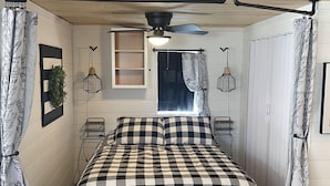Un dormitorio con cubrecama a cuadros, ventilador de techo, ventana con vistas y una puerta.