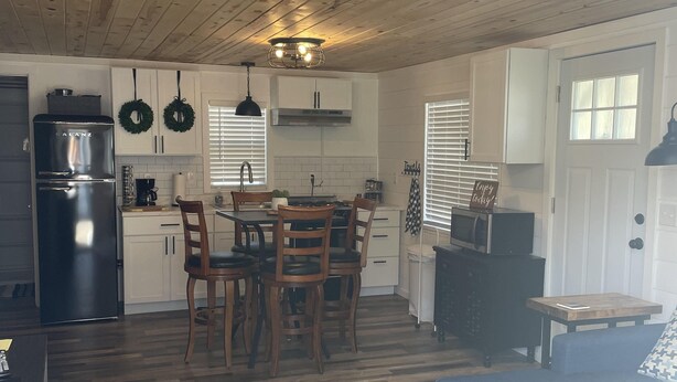 Una cocina moderna con armarios blancos, un refrigerador negro y un comedor con sillas de madera y una mesa.