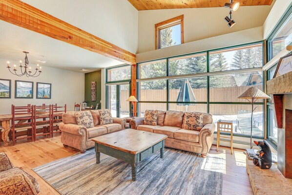 A spacious living room with a large sectional sofa, wooden flooring, and large windows offering a view of the outdoors.