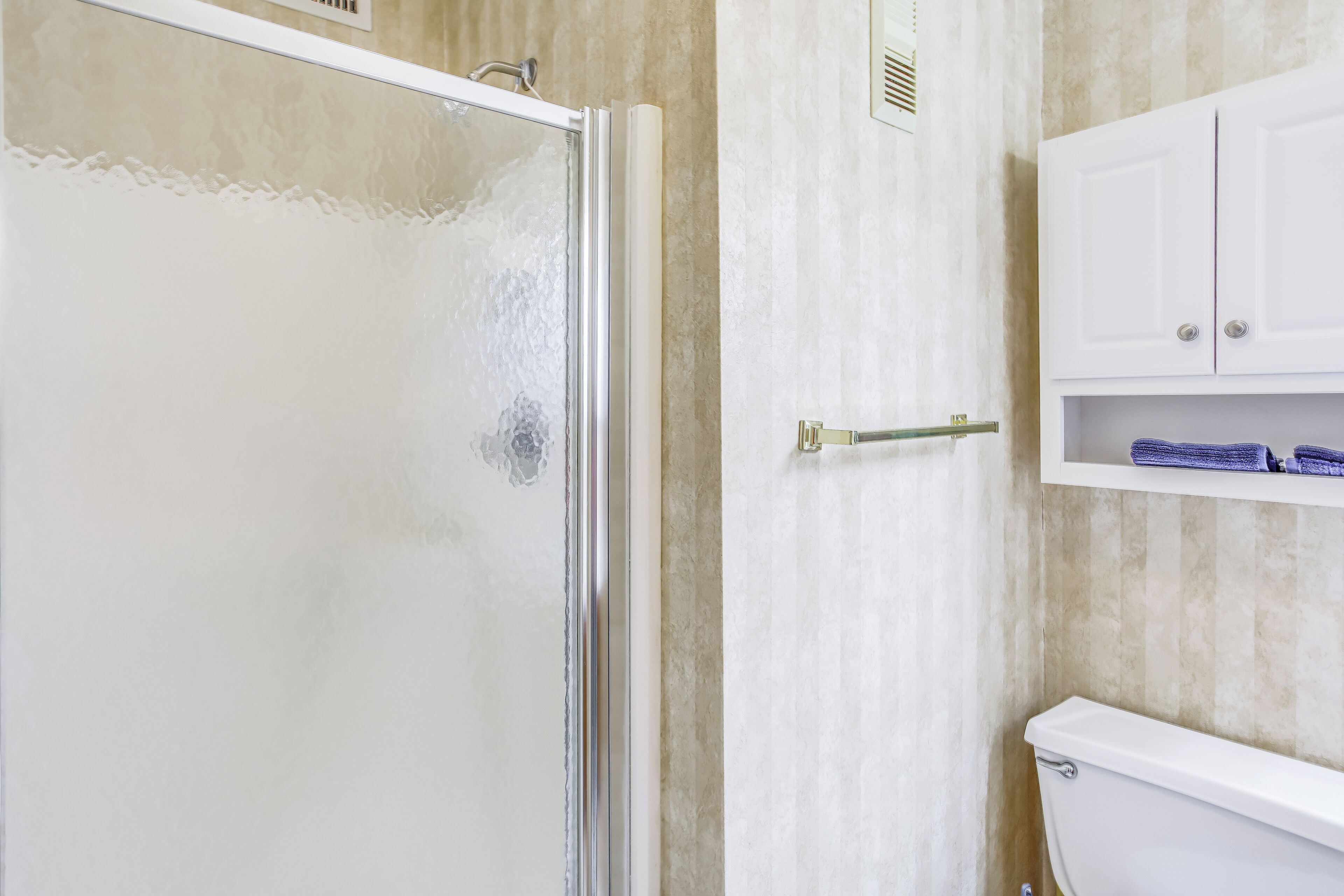 Un bagno con porta doccia in vetro, un WC bianco e un armadietto bianco con asciugamani.
