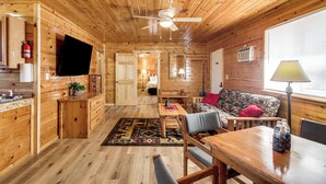 Interior de una cabaña de madera con comedor, sofá y ventilador de techo.