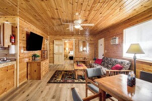 Interior de una cabaña de madera con comedor, sofá y ventilador de techo.