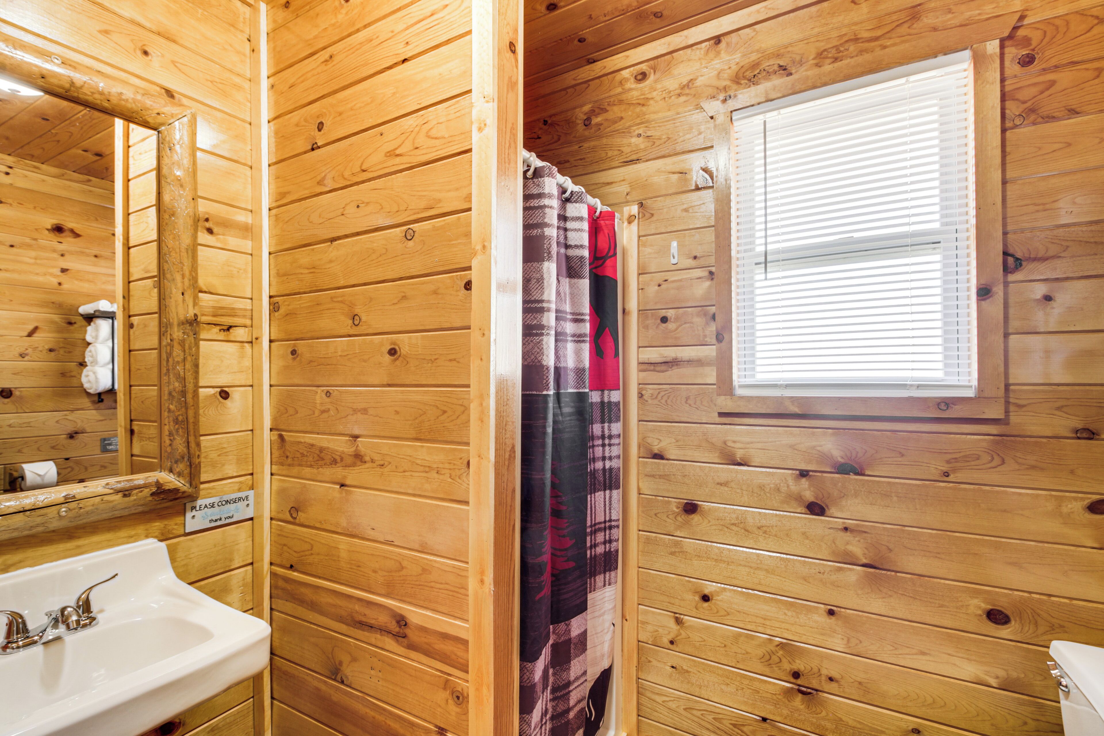 A wooden cabin bathroom with a sink, mirror, and window.