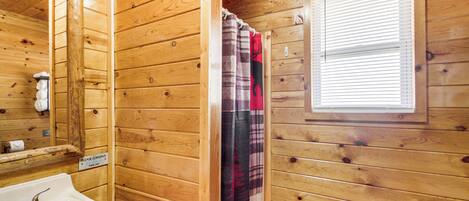 A wooden cabin bathroom with a sink, mirror, and window.