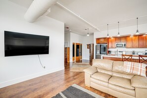 Ein modernes Wohnzimmer mit Flachbildfernseher, einer Ledersofa, Holzböden und einer Küchenzeile mit Holzschränken und einer Mikrowelle.