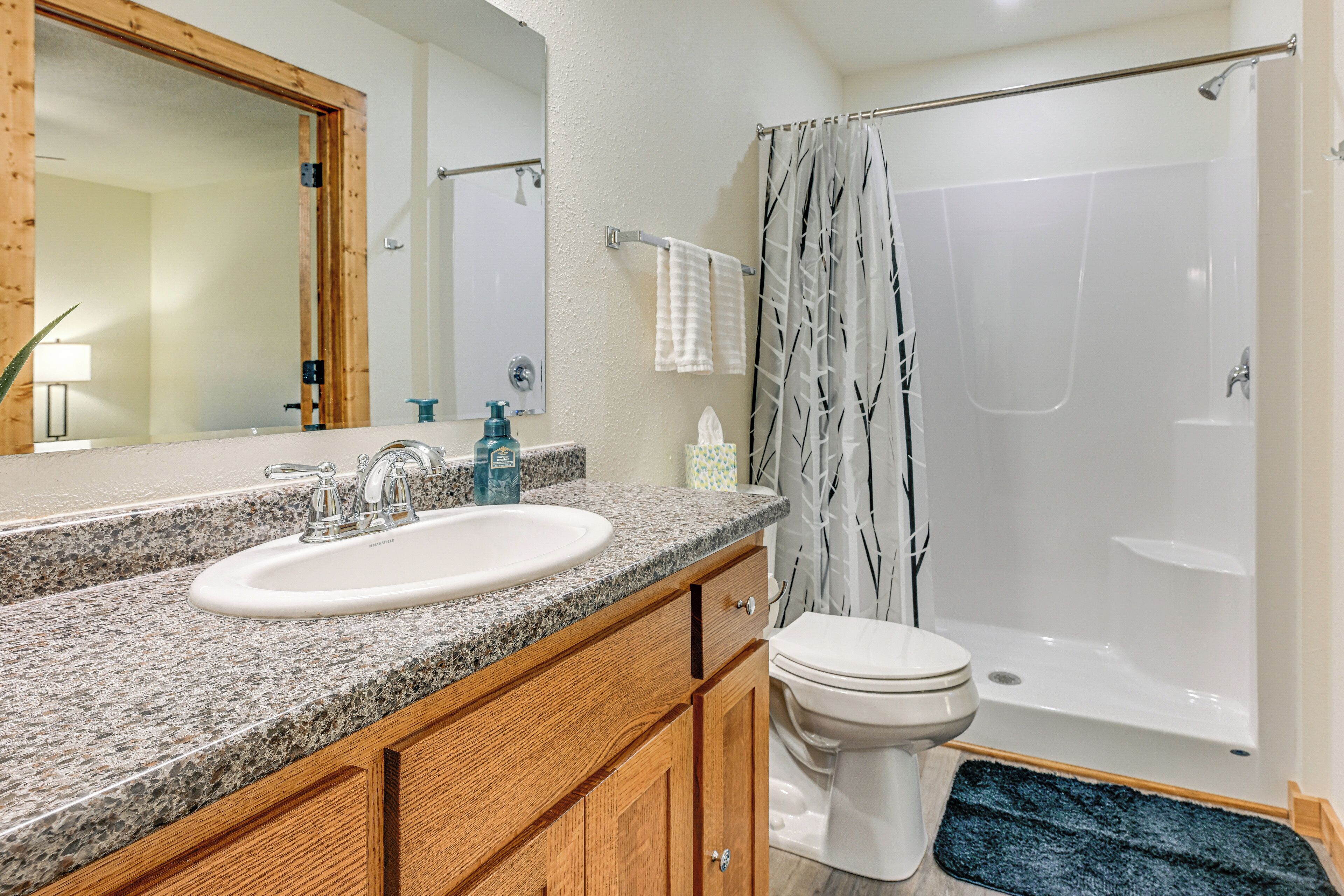 A bathroom with a granite countertop sink, wooden cabinets, a white toilet, and a glass-enclosed shower.