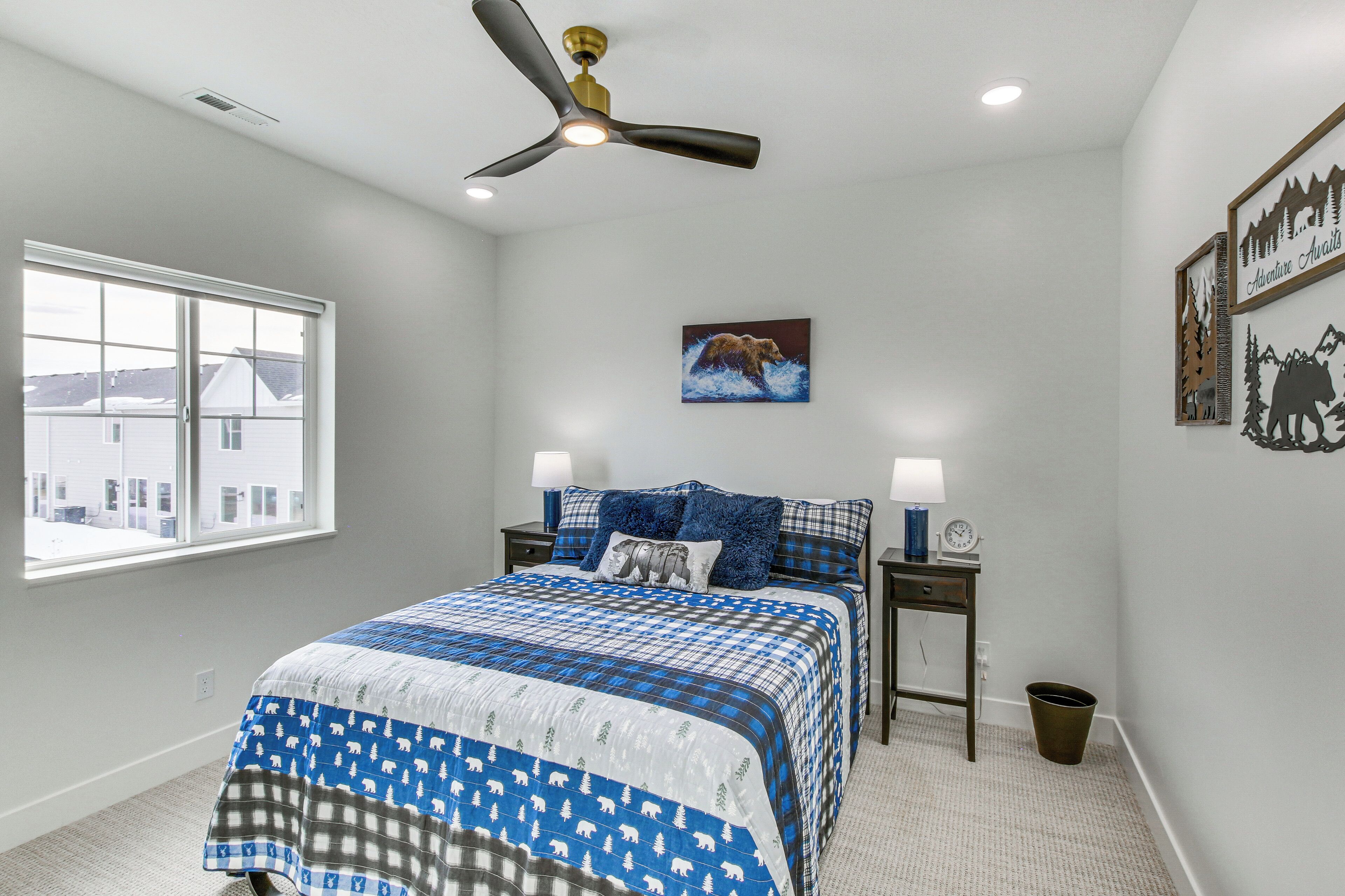 A bedroom with a bed, a ceiling fan, a window, and a wall-mounted picture.