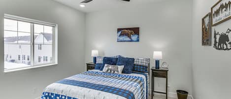 A bedroom with a bed, a ceiling fan, a window, and a wall-mounted picture.