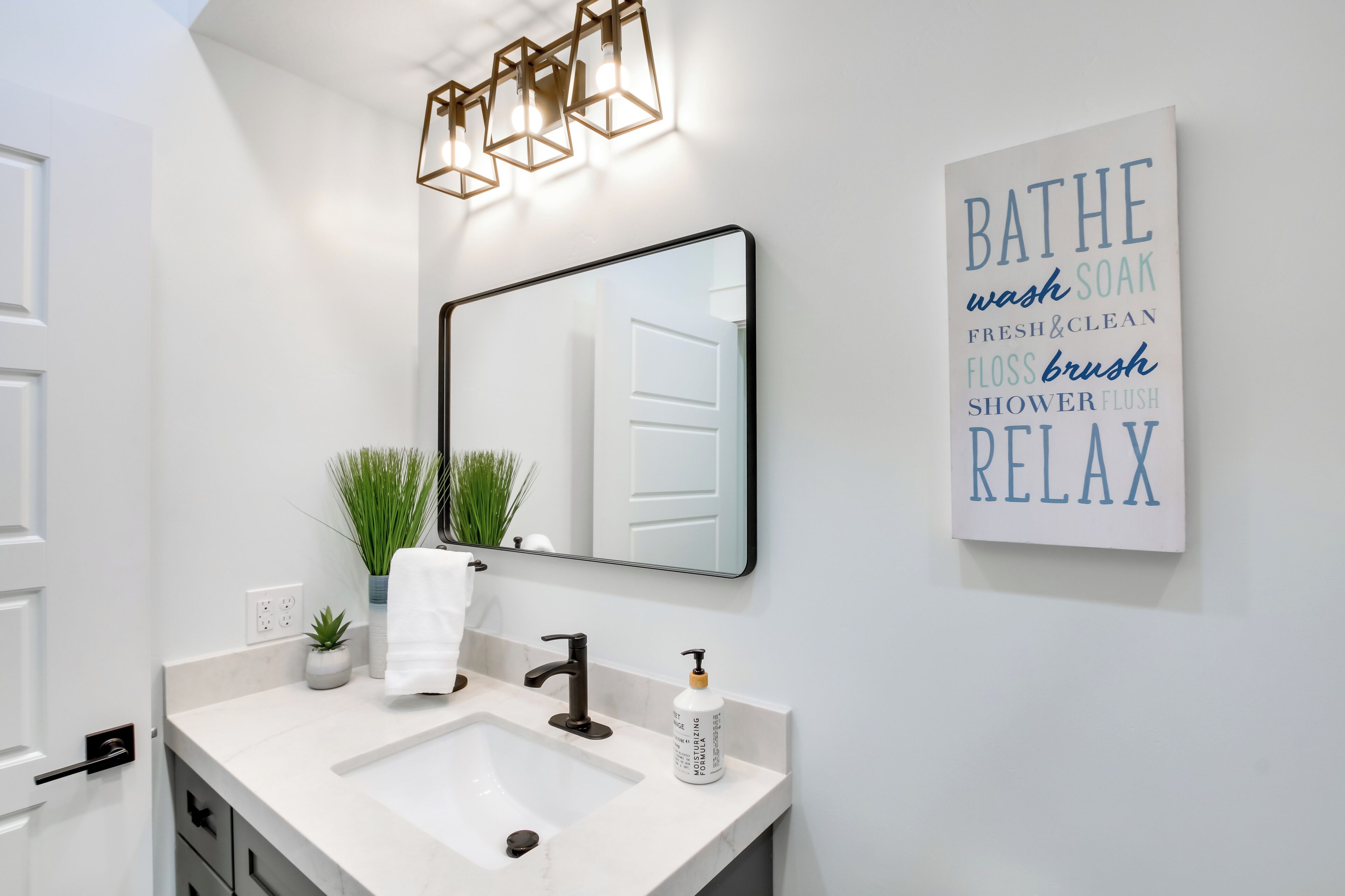 A modern bathroom with a white sink, a mirror, and a wall-mounted light fixture.