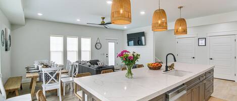 A spacious kitchen with a large island, pendant lighting, and a dining area with wicker chairs.
