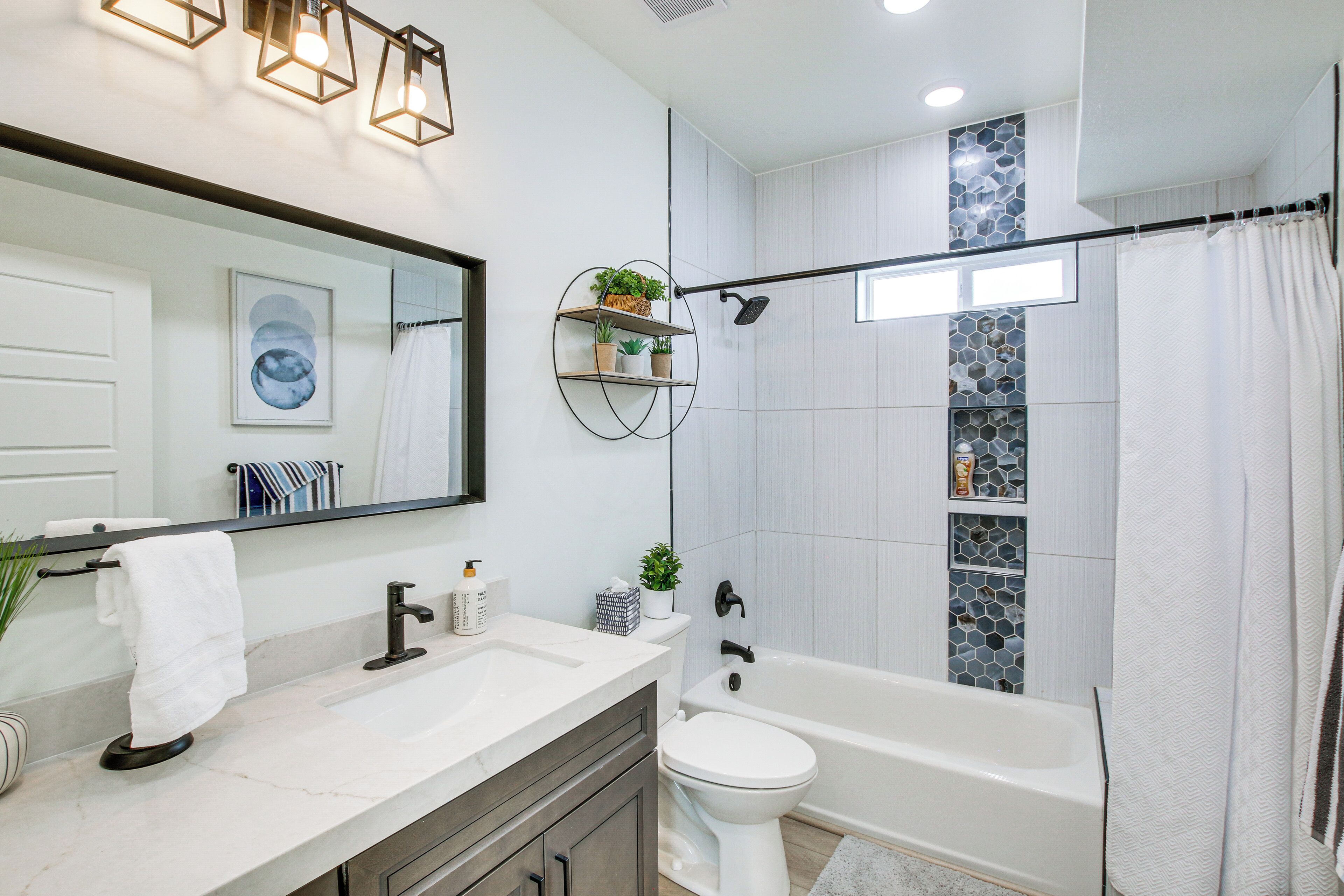 A modern bathroom with a white sink, toilet, and bathtub. There are shelves with plants and toiletries.