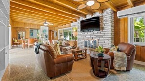 Amplia sala de estar con chimenea de piedra, sofás de cuero y ventilador de techo.