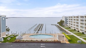 Un hotel frente al agua con piscina, un muelle que se adentra en el agua y un edificio grande con balcones.