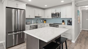 Una cocina moderna con armarios blancos, electrodomésticos de acero inoxidable, una isla de mármol y un salpicadero de azulejos.
