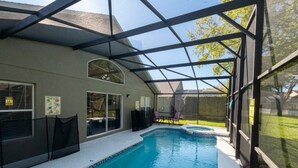 A swimming pool with a glass enclosure, a covered patio area, and a view of the backyard.