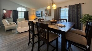 A dining area with a wooden table and chairs, a chandelier, and a television on the wall.