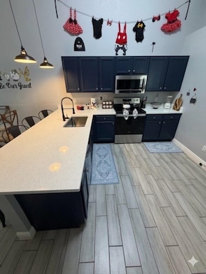 A modern kitchen with dark cabinets, a central island, and a hanging clothes rack. - Private Pool Close To Disney lg Hmslps 8 4 Bedroom Villa by RedAwning (Kissimmee)