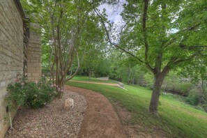 A pathway leading through a garden with a stone wall on one side and trees on the other. - Town Creek Cabin Walk to Main St. (Fredericksburg)