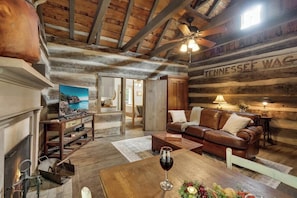 A rustic interior with exposed wooden beams, a leather sofa, a fireplace, and a Tennessee sign. - Town Creek Cabin Walk to Main St. (Fredericksburg)