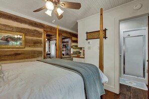 A bedroom with a wooden ceiling, a ceiling fan, a bed with a gray blanket, a door, and a window. - Town Creek Cabin Walk to Main St. (Fredericksburg)