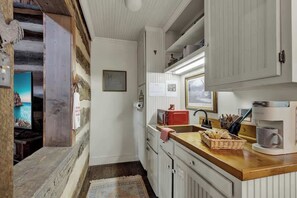A compact kitchen with white cabinets, a wooden countertop, a microwave, a coffee maker, and a small sink. - Town Creek Cabin Walk to Main St. (Fredericksburg)