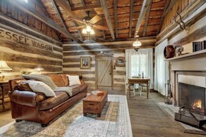 Interior rústico de una cabaña de troncos, con un sofá de cuero, una mesa de centro de madera, chimenea y un comedor.