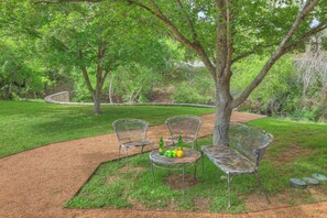 A park setting with a paved path, metal chairs, a metal table, and a bottle of beer.