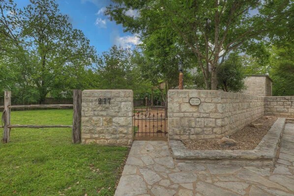Una puerta de piedra con una placa de número, un camino empedrado y un área verde con árboles.