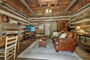 Interior rústico de una cabaña de troncos con una mesa de comedor de madera, sofá de cuero y una chimenea.