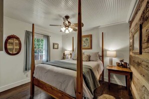 Una cama con dosel, un ventilador de techo, una mesita de noche de madera y un ventanal con cortinas.