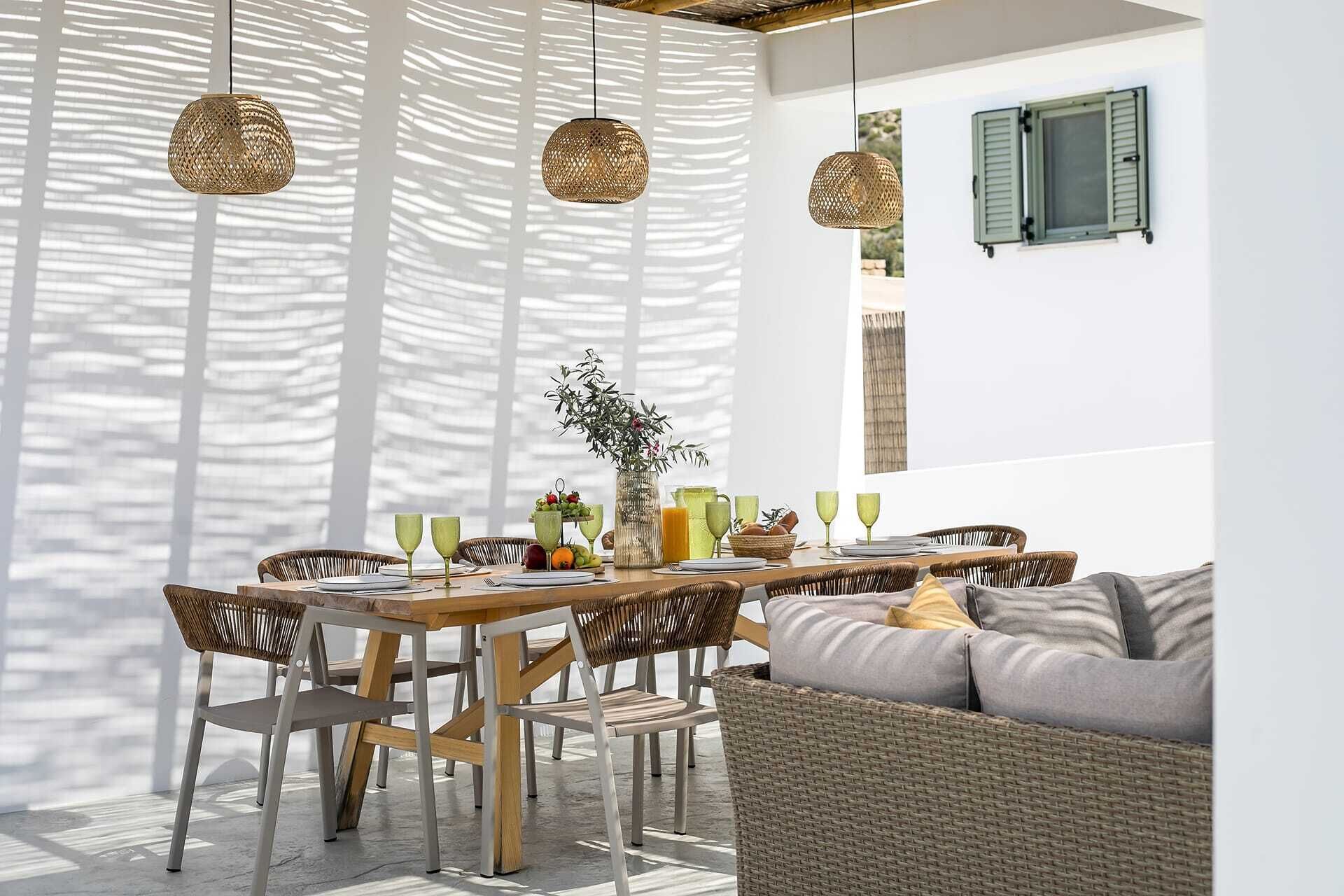 An outdoor dining area with wicker furniture, a wooden table, and hanging wicker lamps.