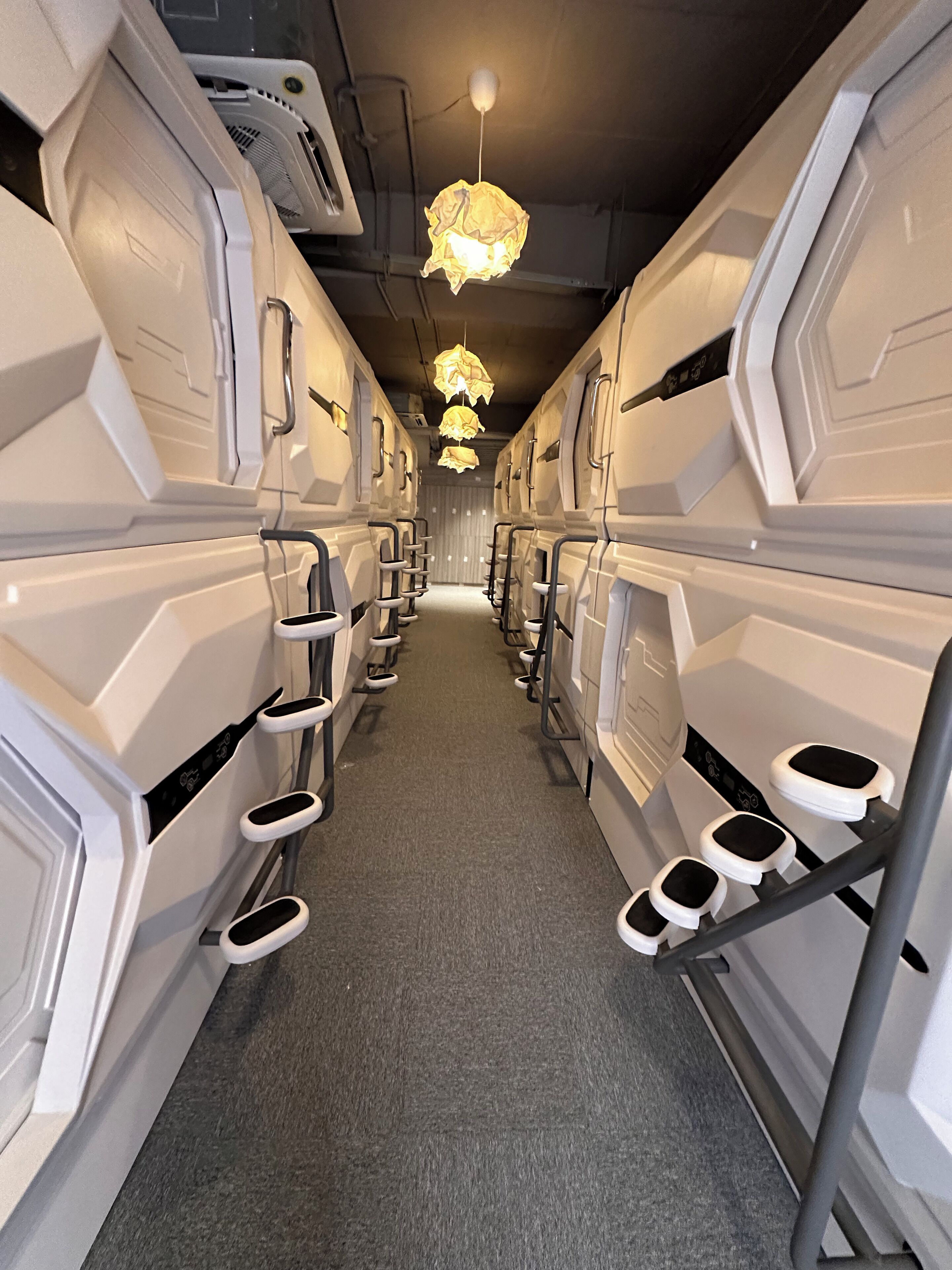 A row of bunk beds with attached storage, a central aisle, and a hanging light fixture.
