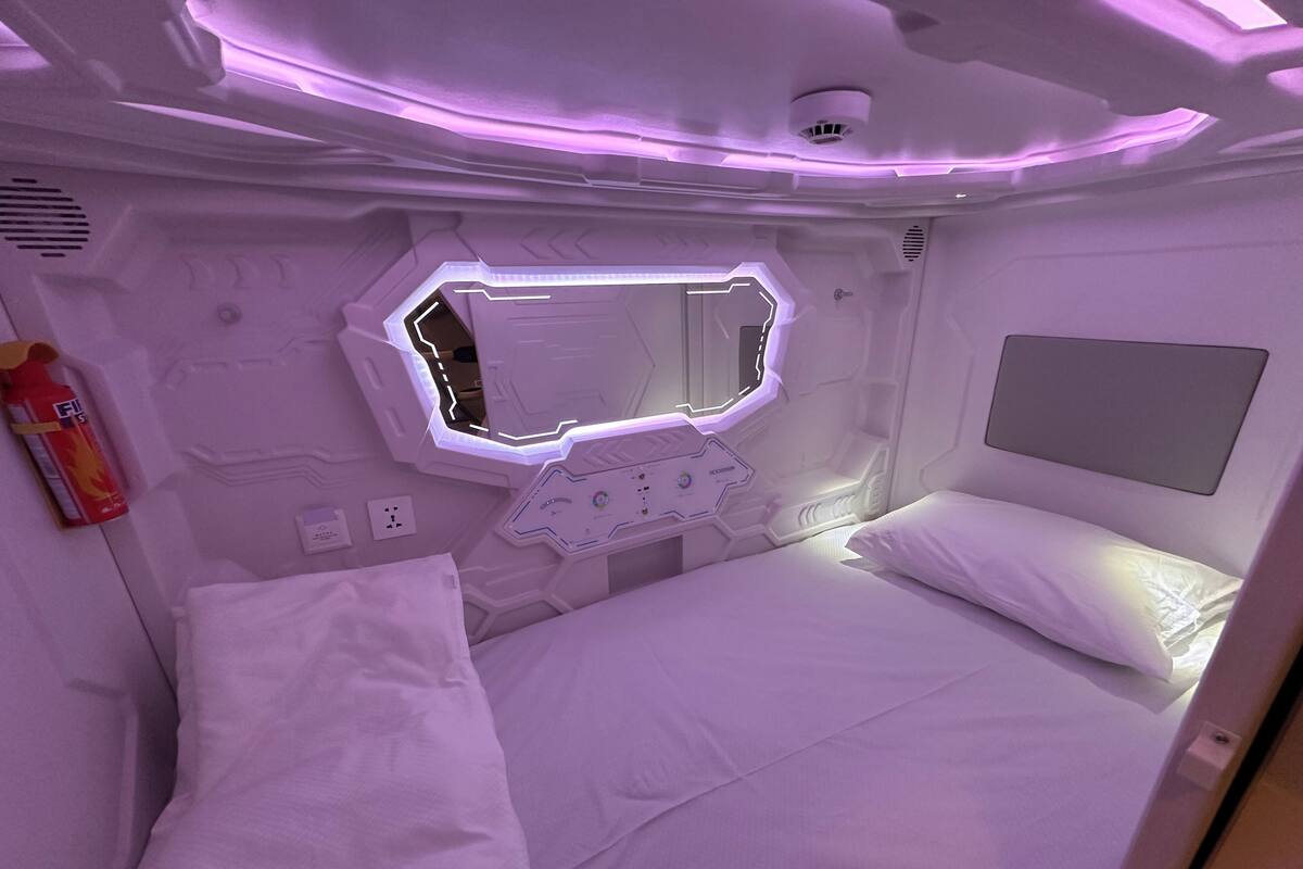 A modern, well-lit room with a bed, a small table, and a wall-mounted mirror.