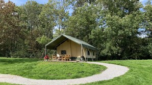 A single-story tent with a green roof and beige walls, surrounded by a gravel path and lush green grass. - Luxe Safaritent, Midden in de Natuur (Hensbroek)