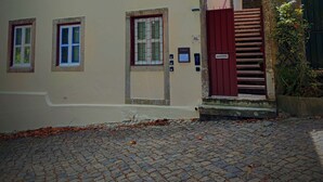 Ein Gebäude mit mehreren Fenstern, einem roten Tor und einem Pflastergrund.
