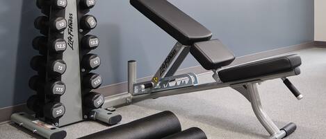A gym with a bench, dumbbells, and a yoga mat.