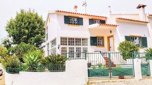 A two-story building with a white facade, green shutters, and a tiled roof.