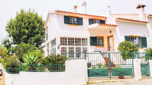 A two-story building with a white facade, green shutters, and a tiled roof.