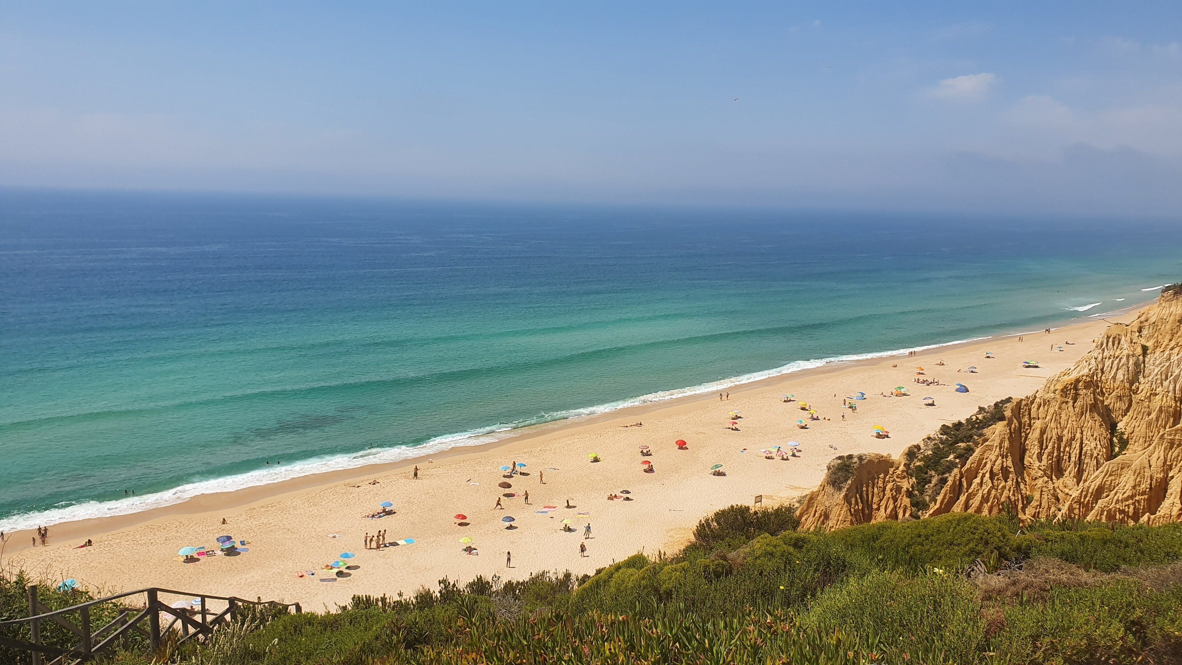 Una playa con vista despejada del océano, orilla arenosa y un acantilado rocoso.