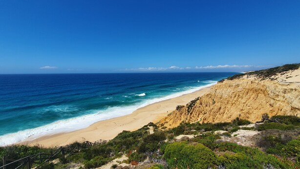 A coastal landscape with a sandy beach, rocky cliffs, and a clear blue sky.
