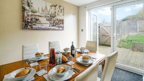 Mesa de comedor dispuesta con platos, tazones, vasos y una botella, con un cuadro de paisaje urbano en la pared.