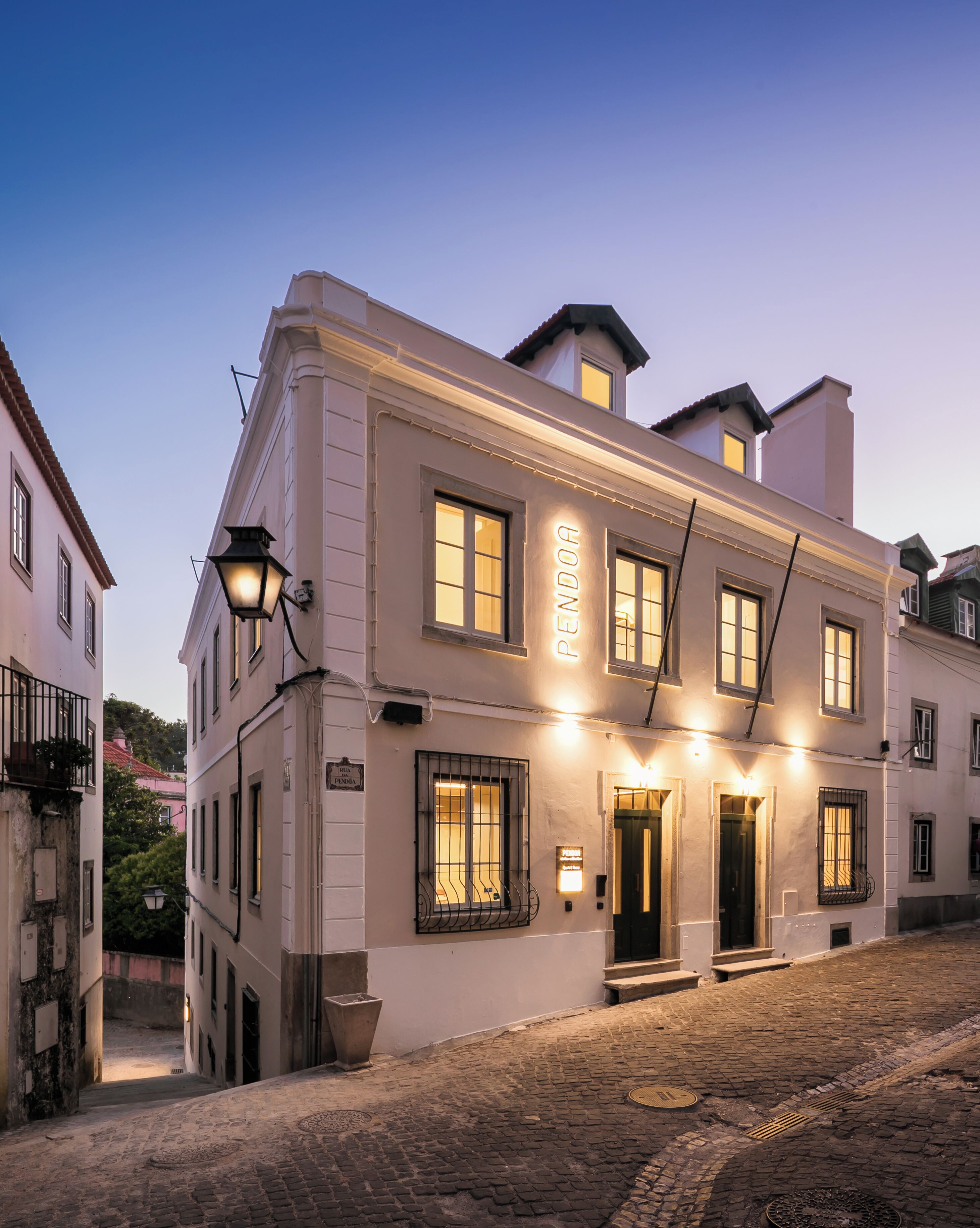 Ein historisches Gebäude mit einer Fassade, auf der 'PENDORA' steht, mehreren Fenstern und einer gepflasterten Straße.