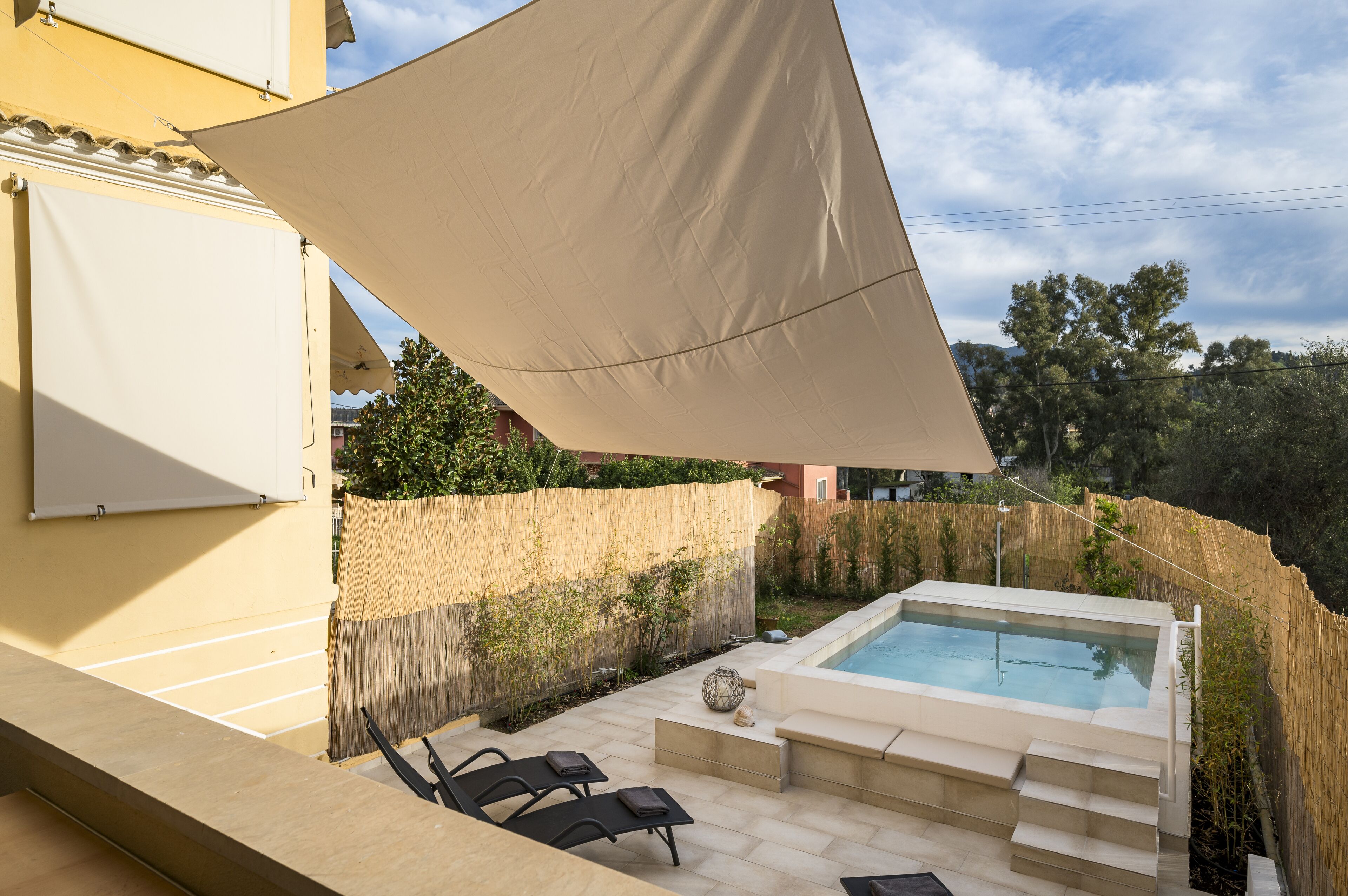 Un espace extérieur privé avec piscine, un jacuzzi, des chaises longues et une grande voile d’ombrage.
